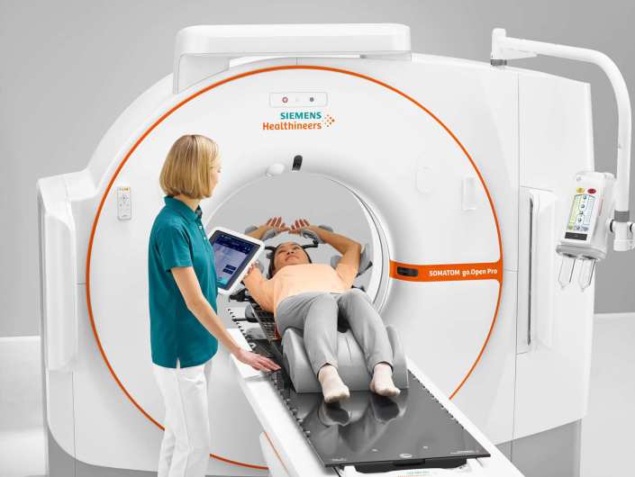 A patient lying in a CT scanner, healthcare professional looking after